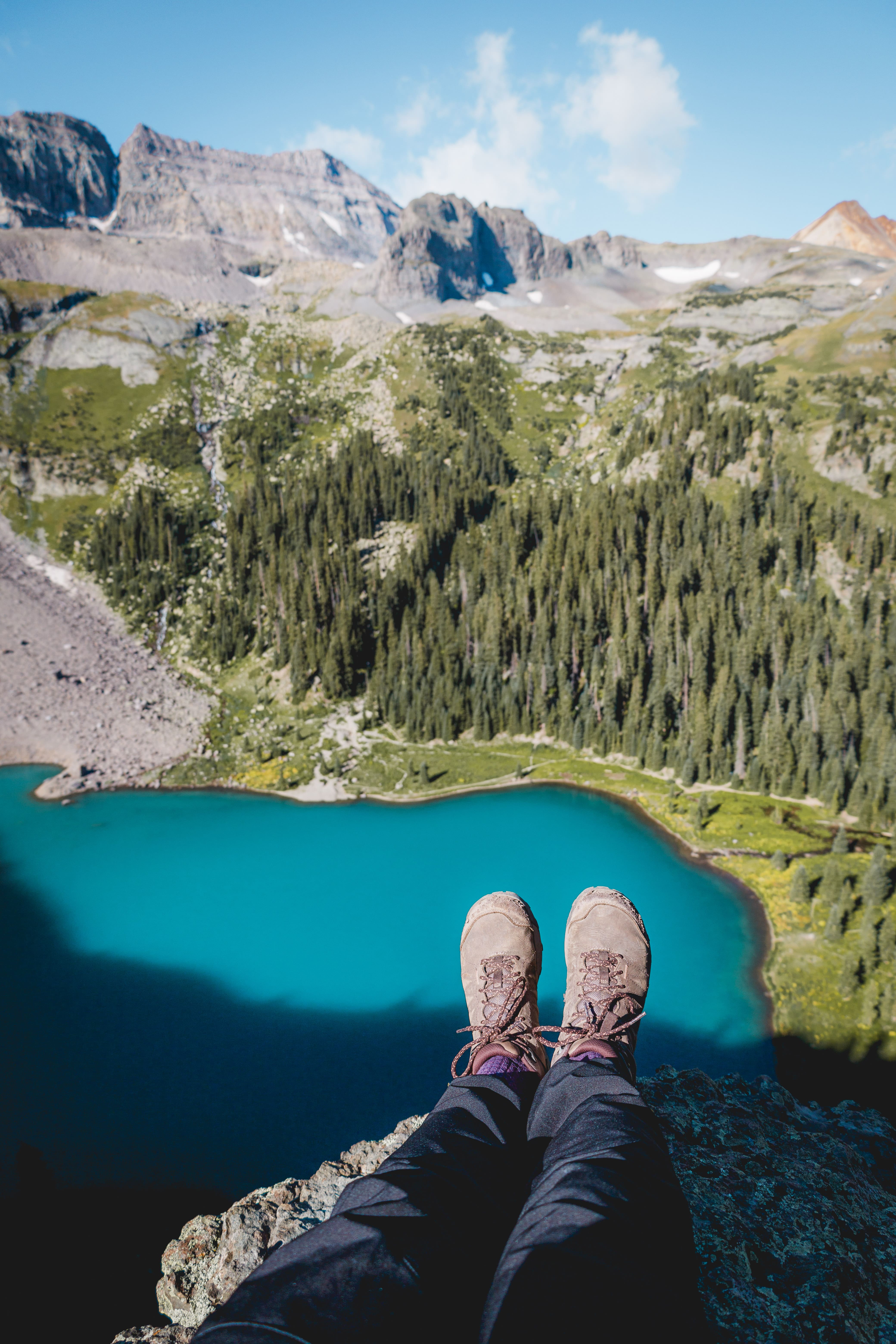 feet hanging off cliff in front of blue lake