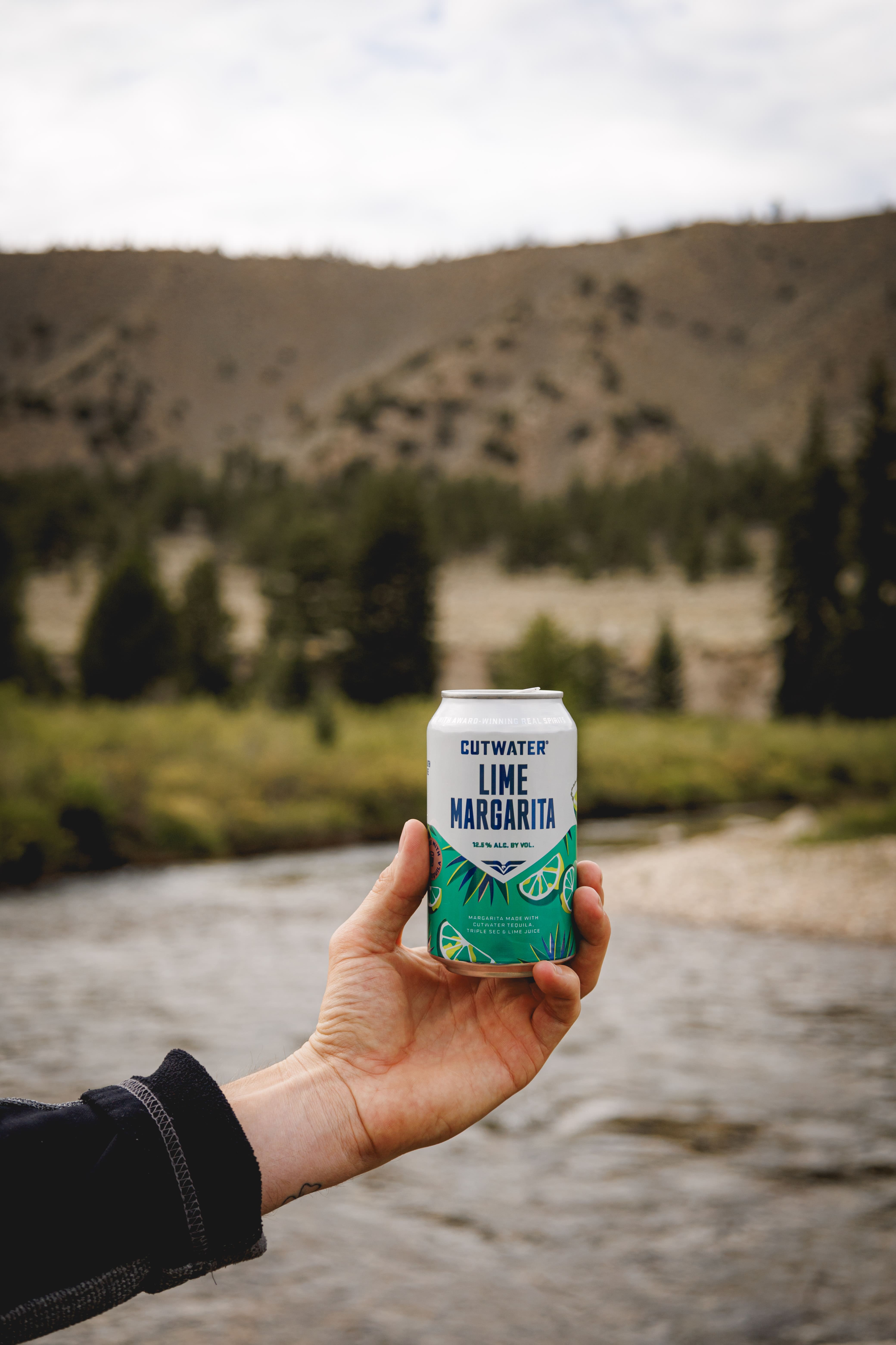 hand holding a can in front of river